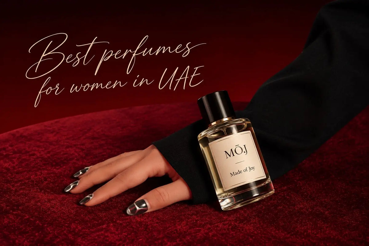 MOJ Made of Joy perfume bottle with black cap resting against a woman's hand in a black sleeve with silver nail art on red velvet, with the words Best perfumes for women in UAE in script