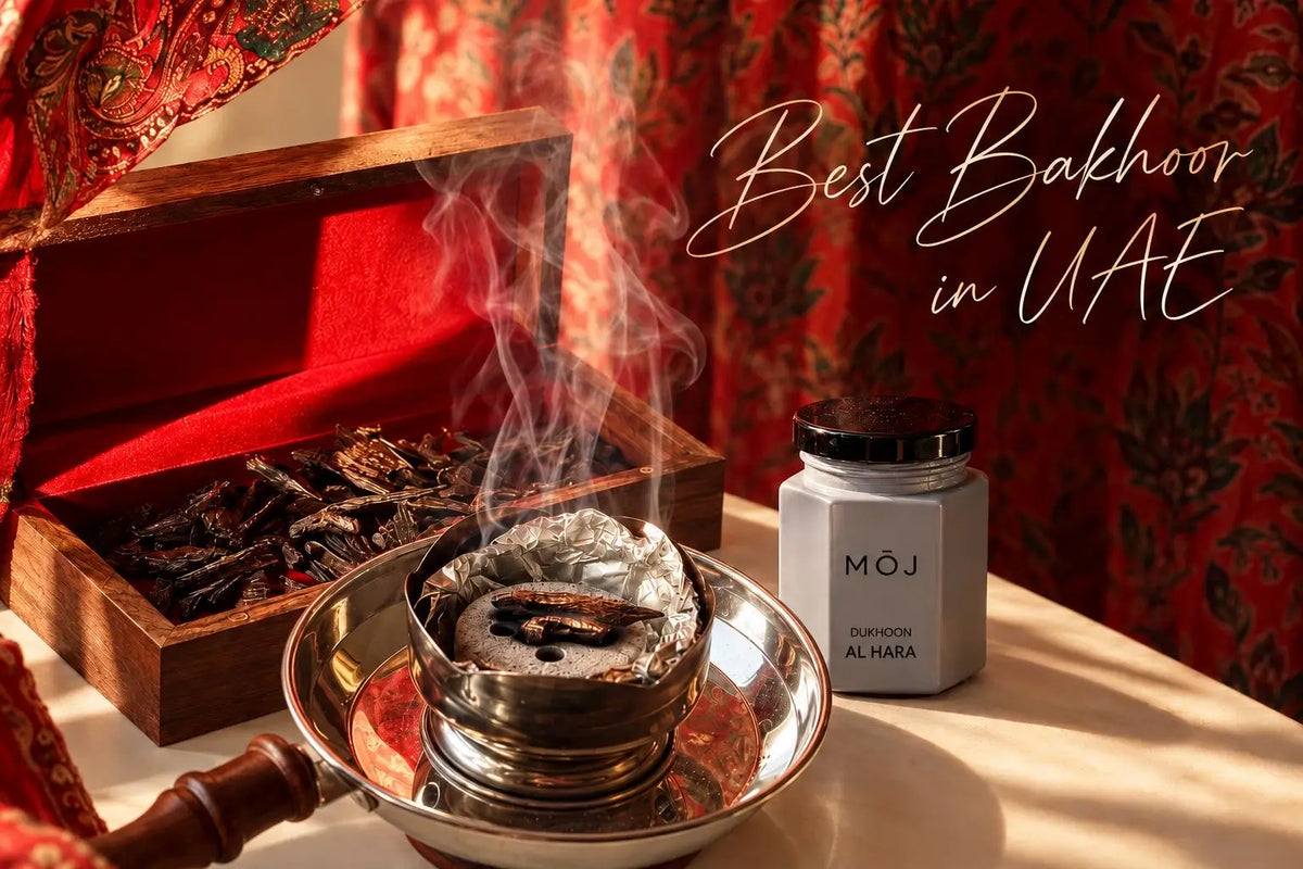 MOJ Dukhoon Al Hara jar beside a smoking bakhoor burner and an open wooden box of oud chips on a table with red patterned curtains, Best Bakhoor in UAE