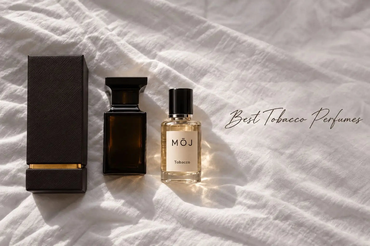MOJ Tobacco perfume bottle beside a dark brown glass bottle and its textured box on white linen in sunlight, with the words Best Tobacco Perfumes
